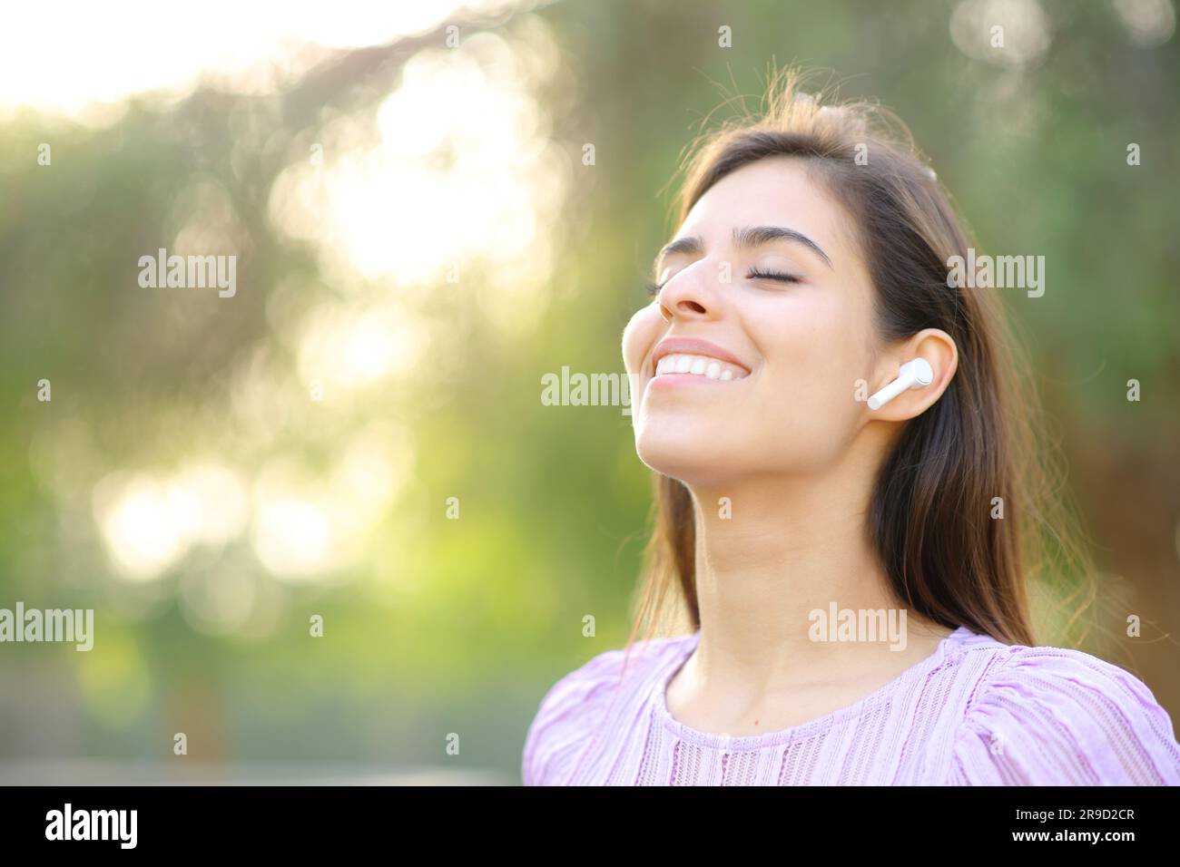 Glückliche Frau, die frische Luft atmet und Ohrstöpsel in einem grünen Park trägt Stockfoto