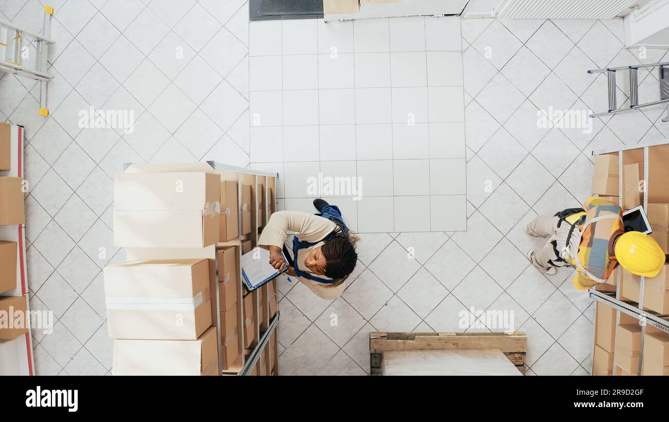 afroamerikanische Kollegen organisieren Lagerbestände auf Regalen und planen den Bestellvertrieb für das Einzelhandelsmanagement. Junge Mitarbeiter, die mit Waren in Kartons oder Containern arbeiten. Drohnenansicht. Stockfoto