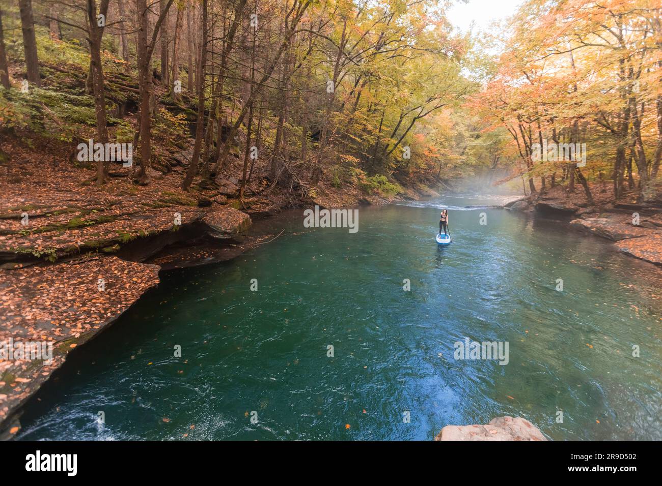 Frau paddelt in einer Herbstszene auf einem klaren Fluss Stockfoto