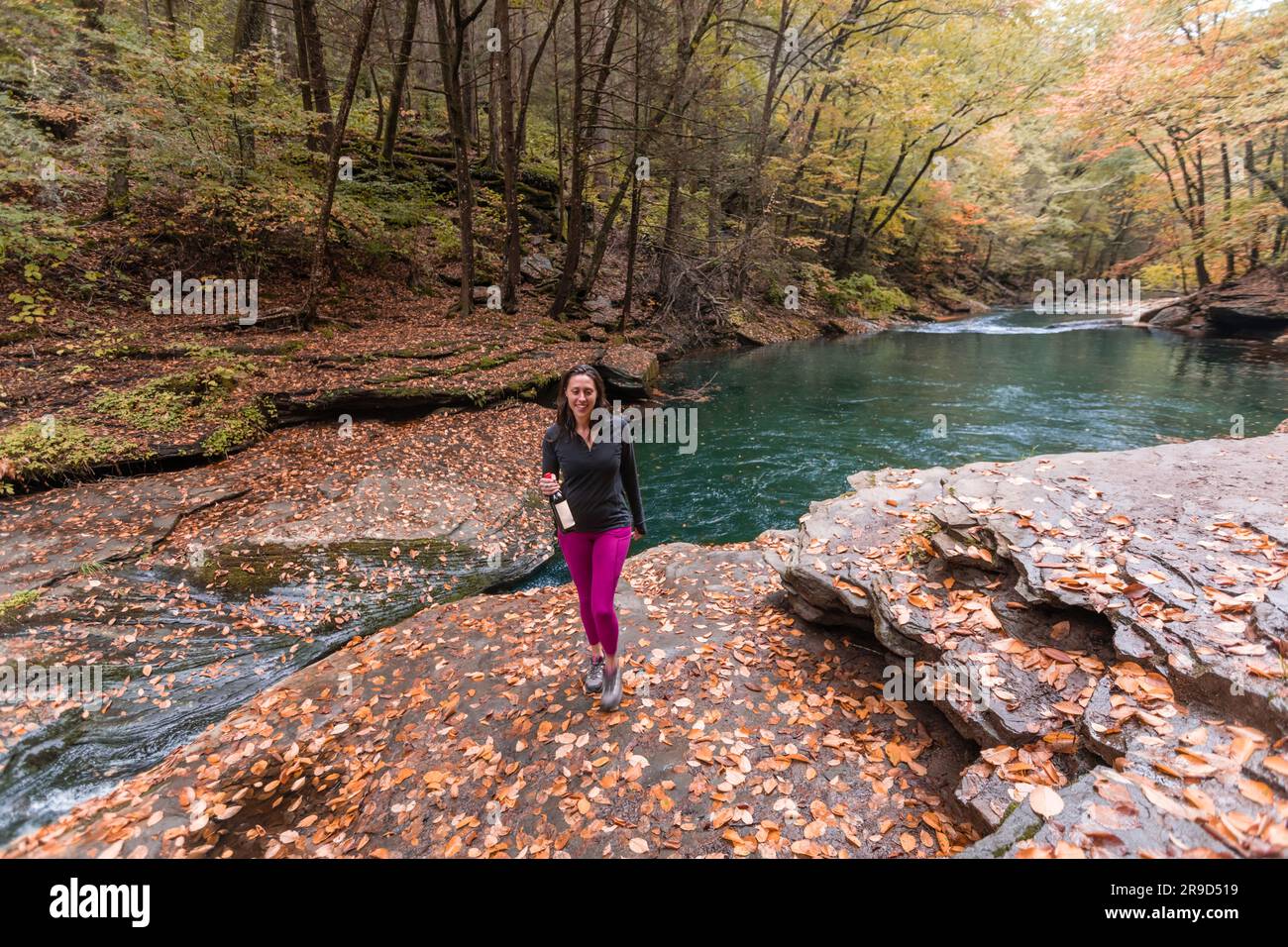 Eine Frau, die in einer Herbstszene an einem Fluss mit Bier spaziert Stockfoto