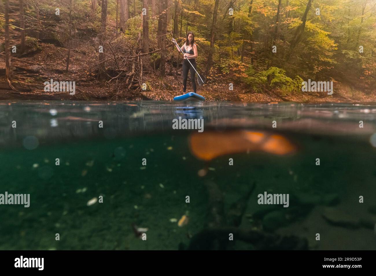 Frau paddelt in einer Herbstszene auf einem klaren Fluss Stockfoto