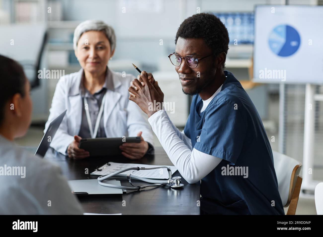 Konzentrieren Sie sich auf junge afroamerikanische Assistentin in Uniform, die eine Kollegin ansieht, während sie während des Gesprächs ihren Standpunkt anhört Stockfoto