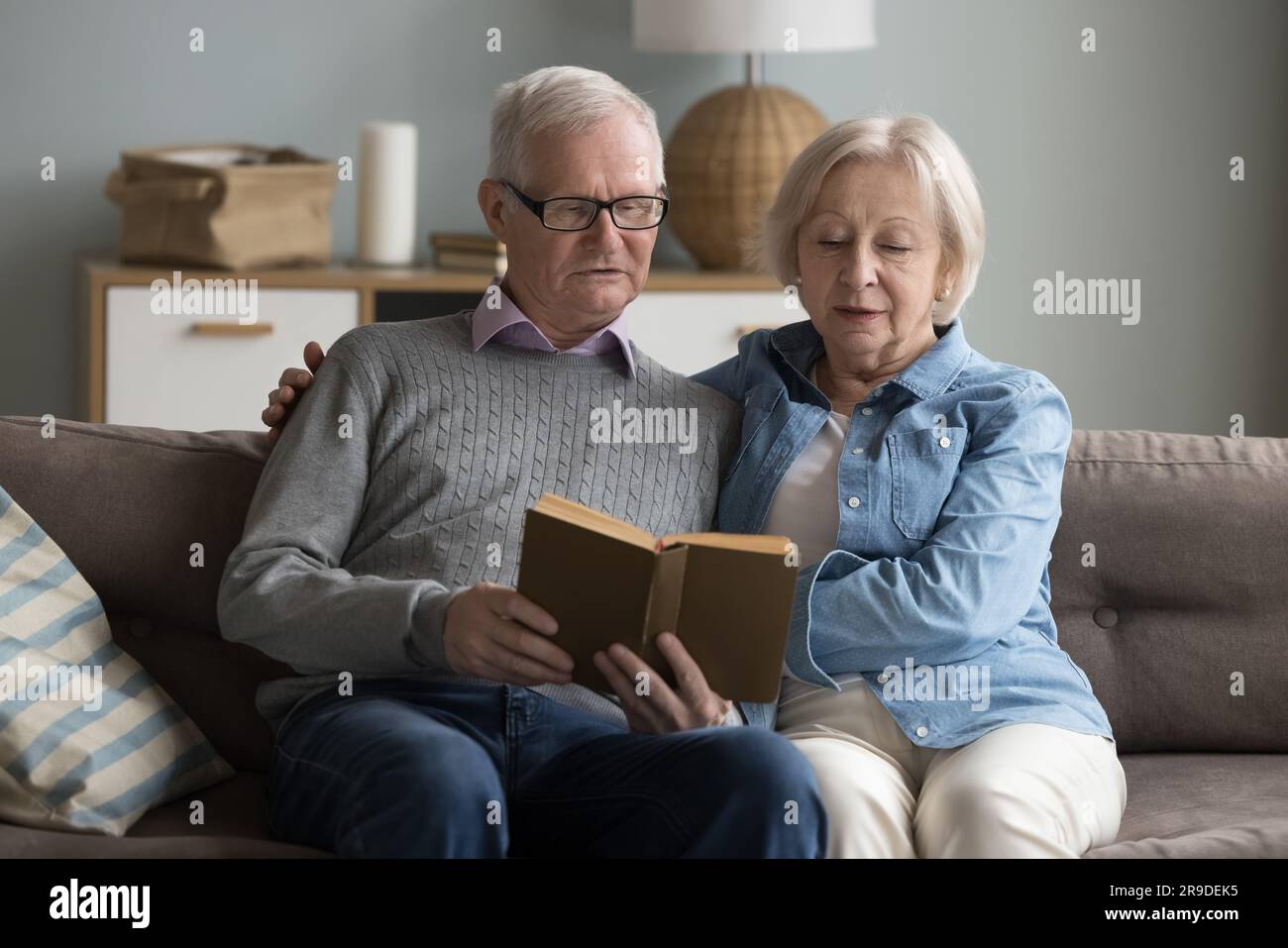 Fokussierte, reife Ehepartner, die zu Hause zusammen ein Buch lesen Stockfoto