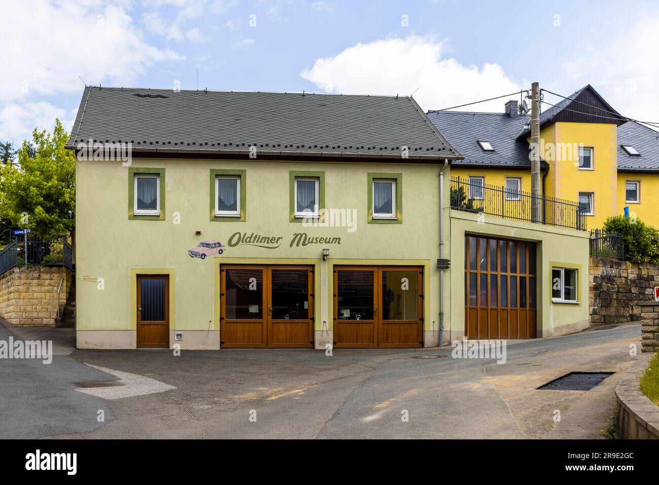 Das Oldtimer-Museum in Schöna, Sachsen, Deutschland, befindet sich in einem hellgrünen Gebäude mit grün gerahmten Fenstern. Ein lackierter Oldtimer schmückt die Fassade neben der Beschriftung. Stockfoto