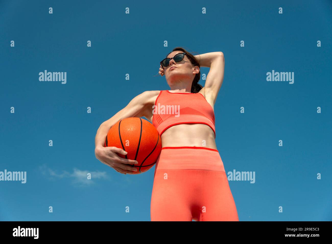 Sportliche Frau mit einem Basketball, draußen mit blauem Himmel Stockfoto