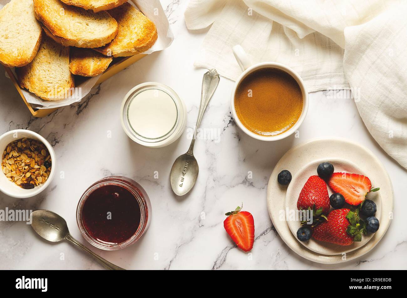 Einfacher Joghurt, frisches Obst, Erdbeermarmelade, eine Schüssel Müsli und Toastbrotscheiben mit einer weißen Serviette auf marmoriertem Hintergrund. Draufsicht. Stockfoto