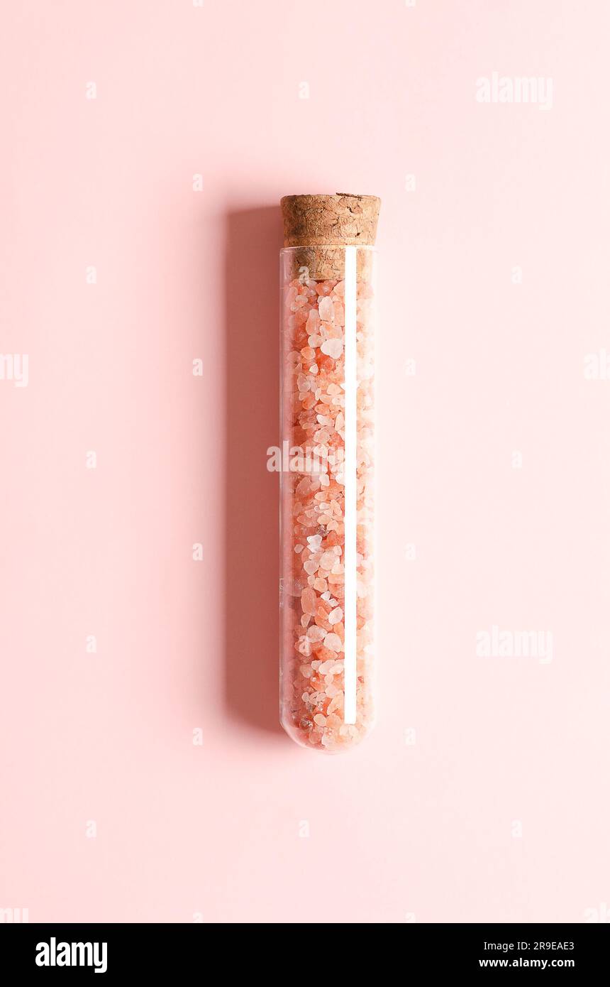 Rosa Himalaya-Salz in einem Glasbehälter mit Kork auf rosa Hintergrund. Vertikales Format. Stockfoto