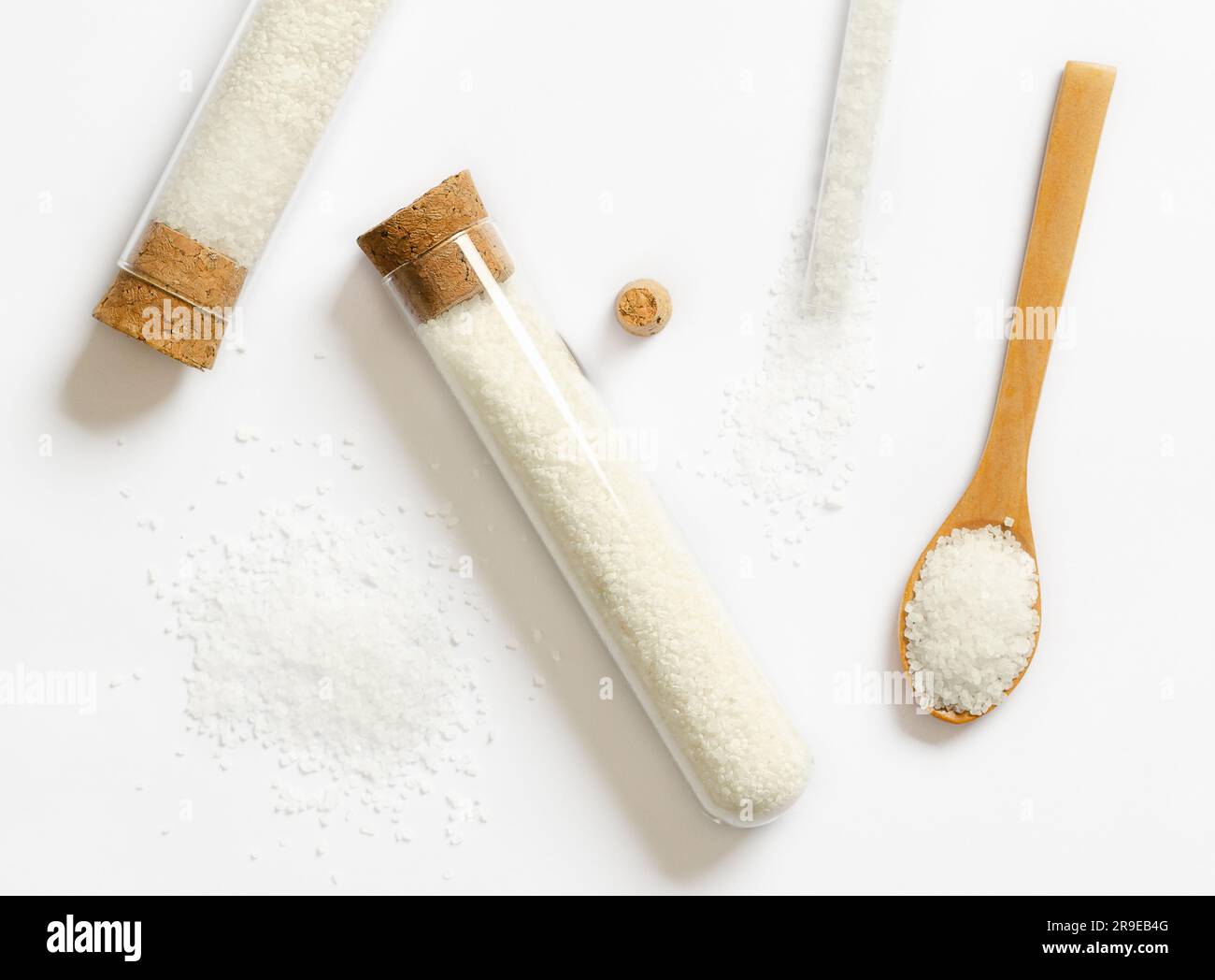 Grobes Salz in Glasflaschen und Holzlöffel auf weißem Hintergrund. Stockfoto