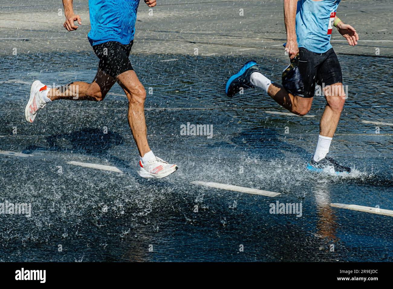 Zwei männliche Läufer laufen ein Marathonrennen in einer Wasserstation, einer Pfütze und Spritzwasser Stockfoto