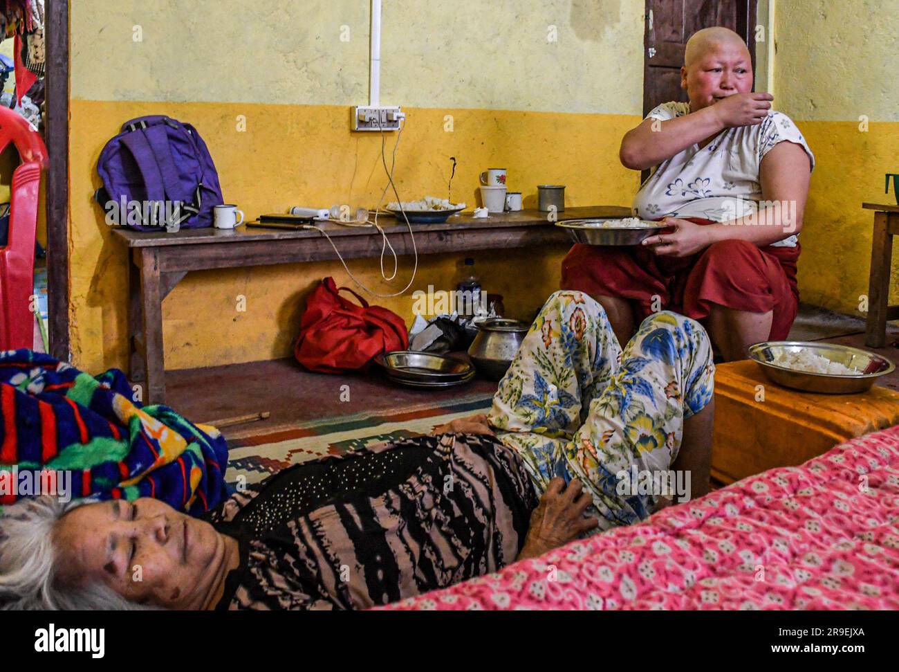 Krebspatientin Chinkhothang Baite (47) isst zu Mittag, während ihre kranke Mutter in einem Hilfslager im Dorf Rengkia auf einem Bett liegt. Am 3. Mai 2023 brach im nordöstlichen indischen Bundesstaat Manipur ein ethnischer Konflikt zwischen dem Volk der Meitei, das mehrheitlich im Imphal-Tal lebt, und den Stammesgemeinschaften in den umliegenden Bergen, einschließlich Kuki und Zo, aus. Mindestens 109 Menschen sind bei ethnisch motivierter Gewalt zwischen der Meitei und den Kuki im indischen Bundesstaat Manipur ums Leben gekommen und über 300 wurden verletzt. Stockfoto