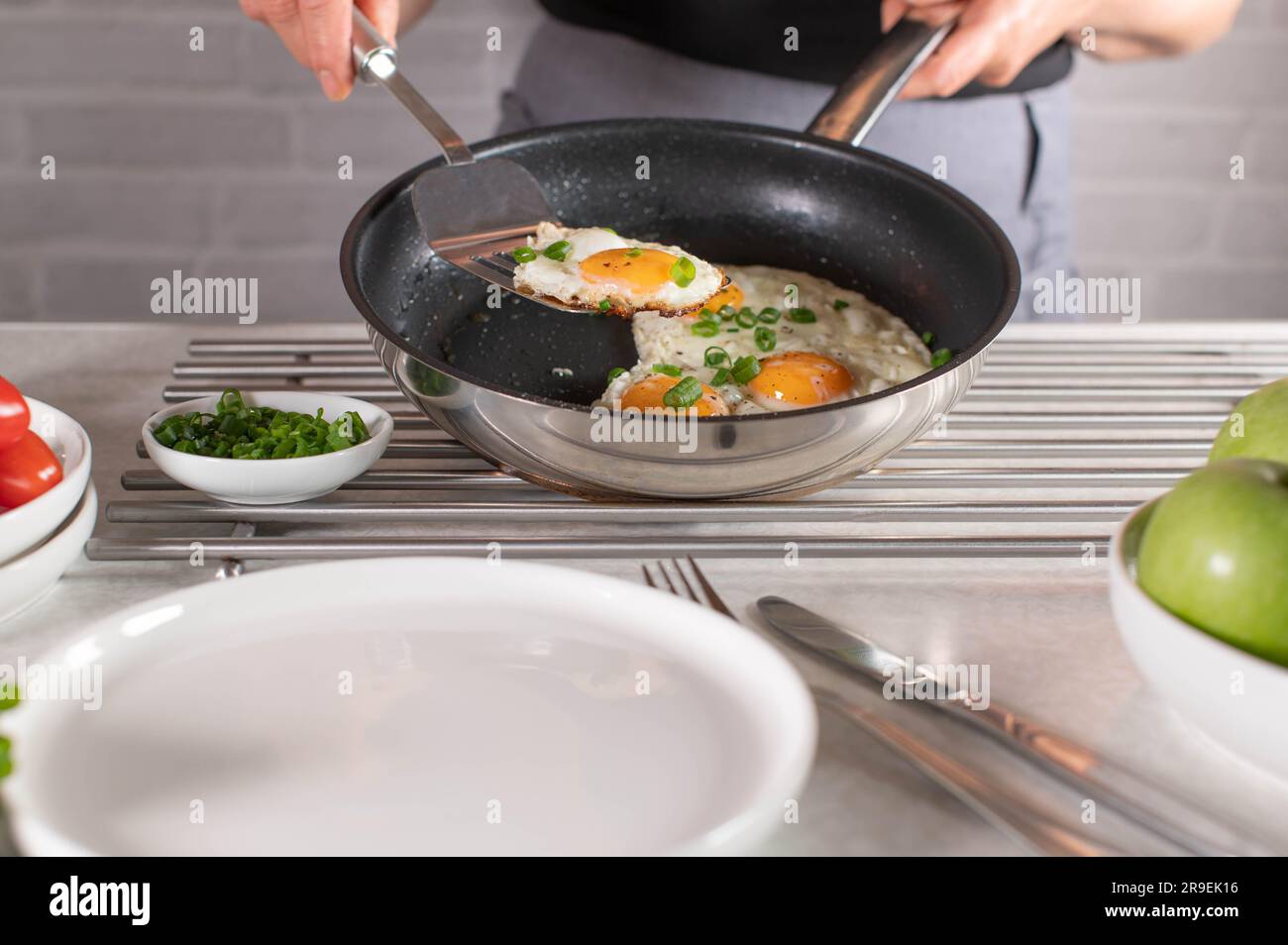 Eine Frau mit Schürze serviert frisch gebratenes Ei in der Pfanne mit einem Teigschaber auf einem Teller Stockfoto