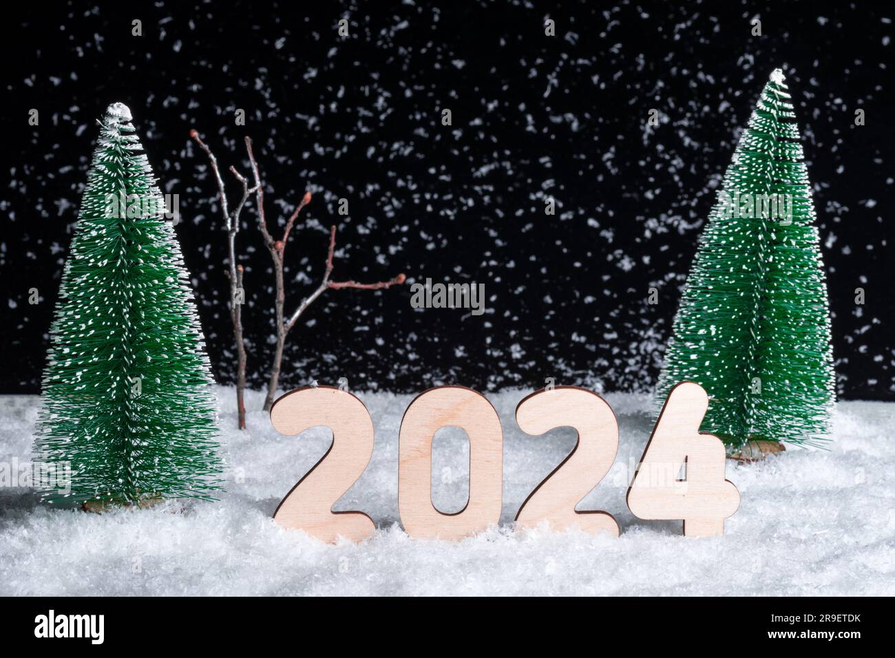 Kreative Neujahrskarte 2024. Eine Komposition aus Holzfiguren des Jahres 2024 in einem verschneiten Wald während eines Schneefalls bei Nacht. Ich warte auf ein Wunder Stockfoto