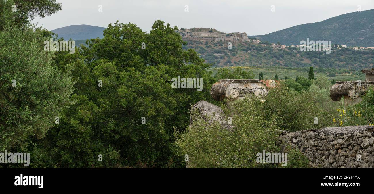 Ein Blick durch ein zerstörtes Steintor mit Ionischen Säulen auf dem Land mit Sträuchern und Bäumen und das Schloss St. Georg in der Ferne, Kefalonia Stockfoto