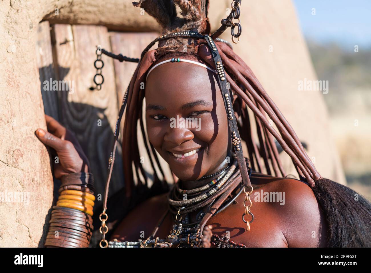 Glückliche lächelnde Himba-Frau, gekleidet im traditionellen Stil in ihrem Dorf in Namibia, Afrika. Stockfoto