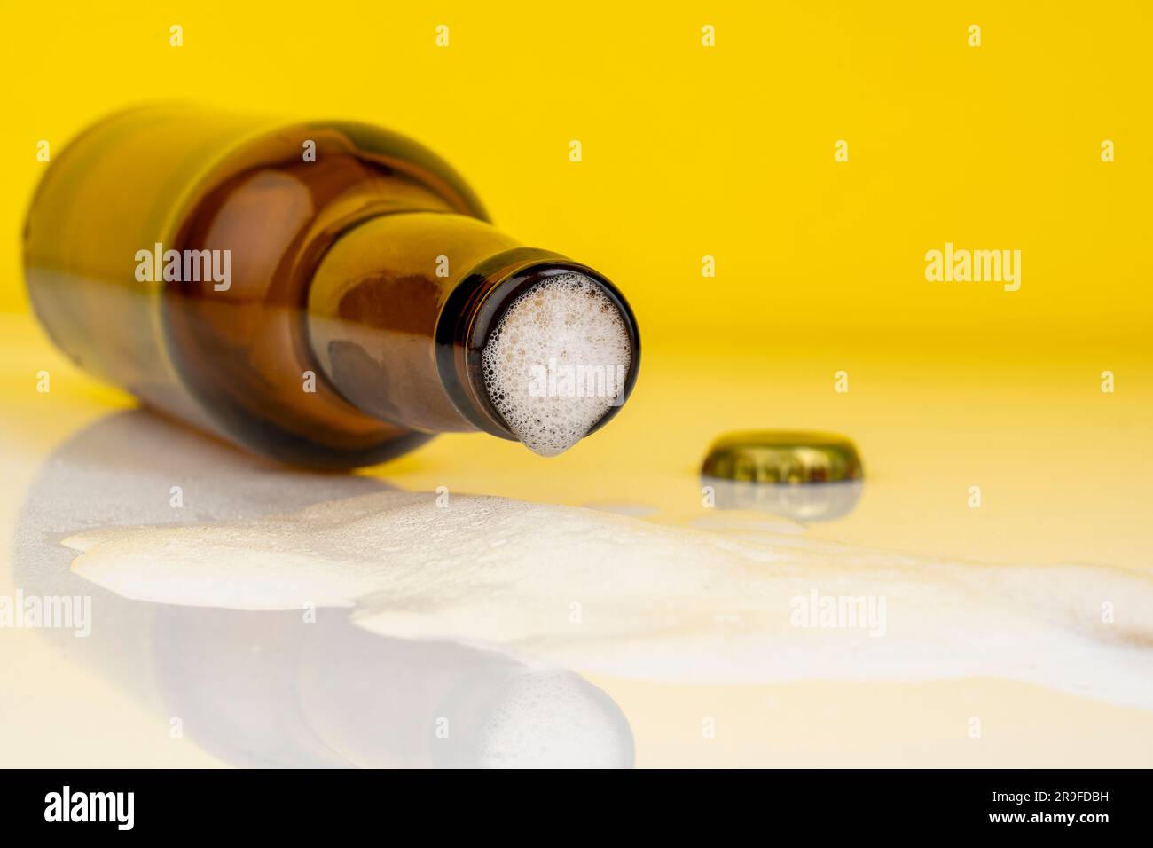 Ein isolierter Shot einer Bierflasche mit offenem Deckel, wobei das Getränk auf der Oberfläche fließt Stockfoto
