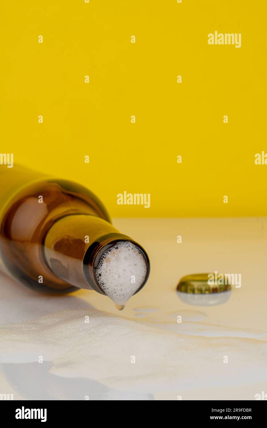 Ein isolierter Shot einer Bierflasche mit offenem Deckel, wobei das Getränk auf der Oberfläche fließt Stockfoto