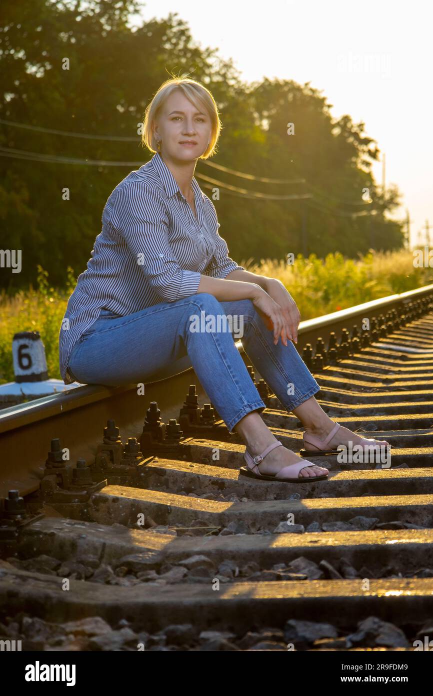 Eine Frau in Jeans sitzt auf einer Eisenbahnstrecke. Stockfoto