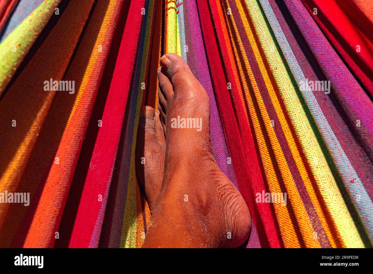 Eine Nahaufnahme, die sich auf die Füße einer farbenfrohen Person konzentriert, die sich gemütlich in einer lebendigen und auffälligen Hängematte ruht. Stockfoto