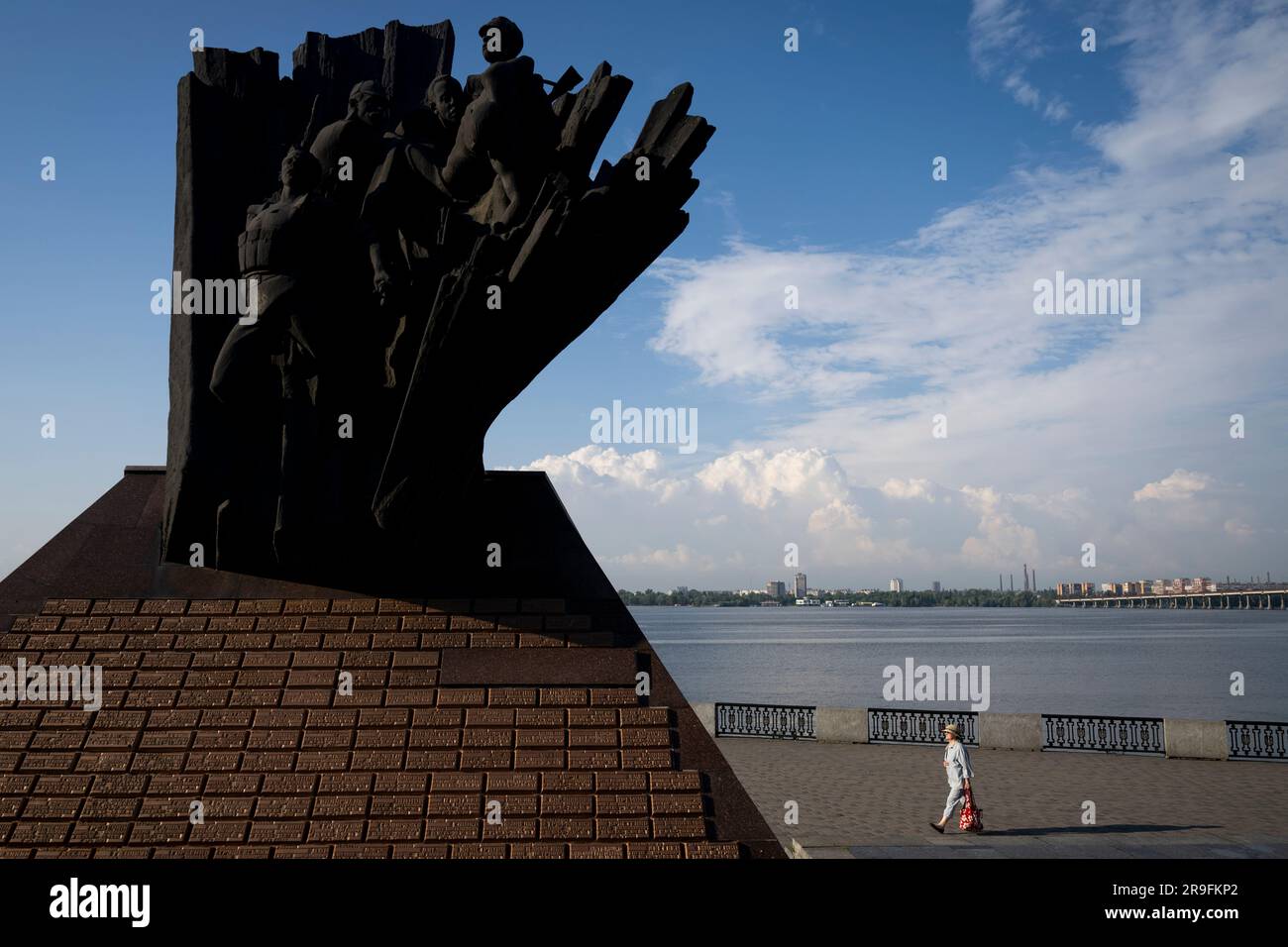 Dnipro, Ukraine. 26. Juni 2023. Eine Frau geht am Ufer des Dnieper River entlang, am 26. Juni 2023, Dnipro, Ukraine. Links sehen Sie eine Gedenkstätte für Soldaten, die in Afghanistan während des Sowjetkrieges von 1979 bis 1989 getötet wurden. Kredit: Ondrej Deml/CTK Photo/Alamy Live News Stockfoto