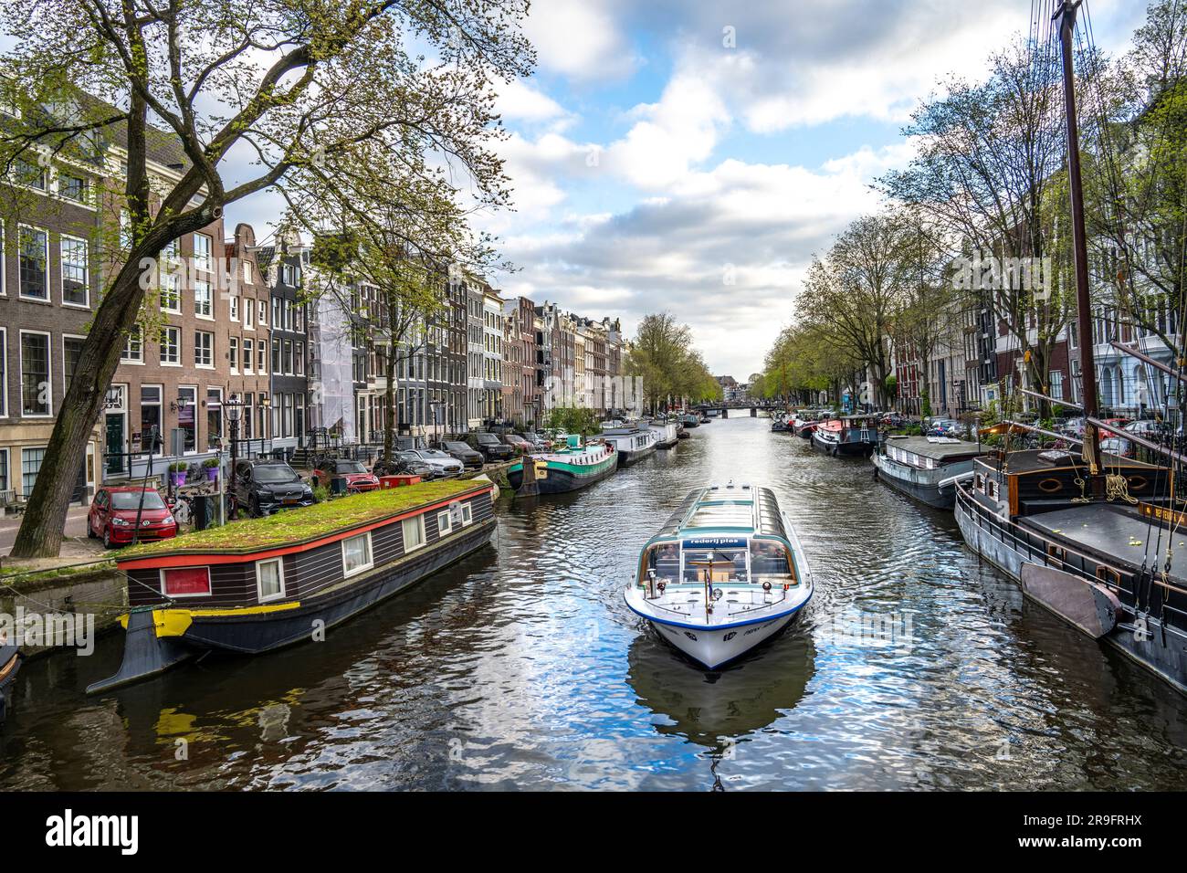 Touristenboot auf einem Kanal unter vielen Hausbooten in Amsterdam Stockfoto