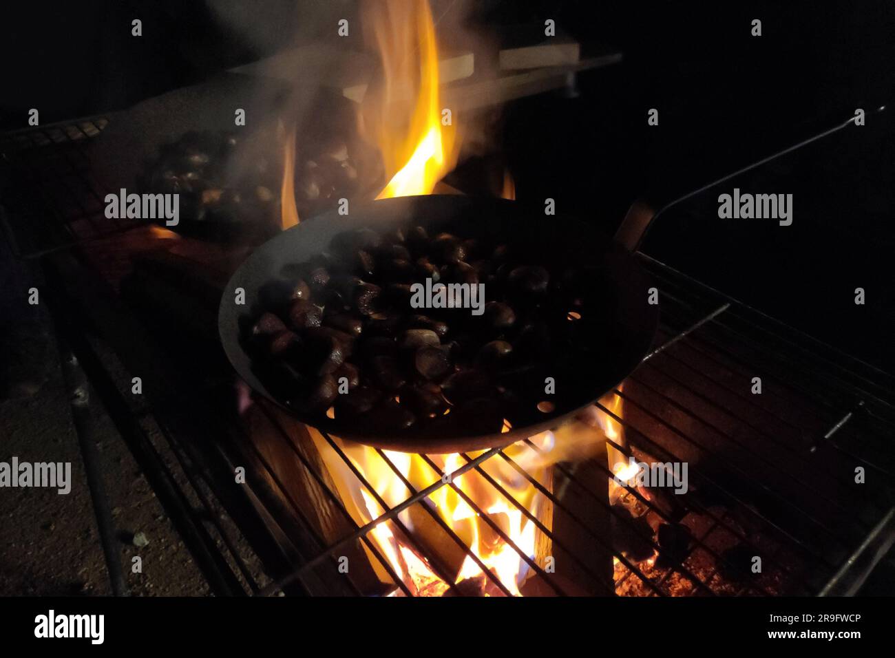 Kastanien in einer durchbohrten Bratpfanne am Feuer bei Nacht rösten. Stockfoto