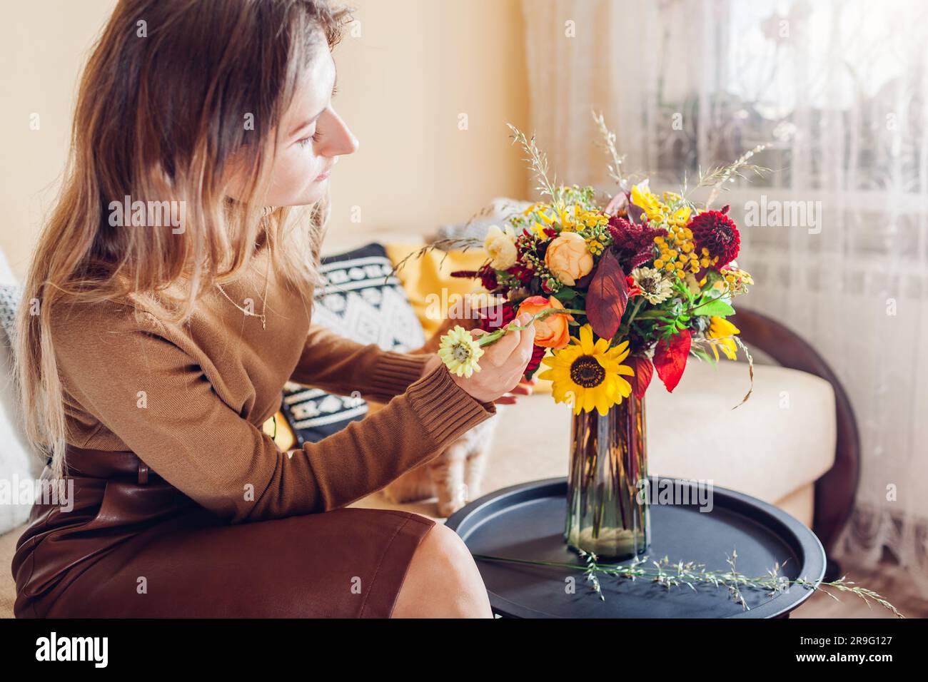 Blumen-Arrangement. Frau macht Herbststrauß aus Sonnenblumen Dahlien Rosen und Zinnien in Vase zu Hause mit Katze. Stockfoto