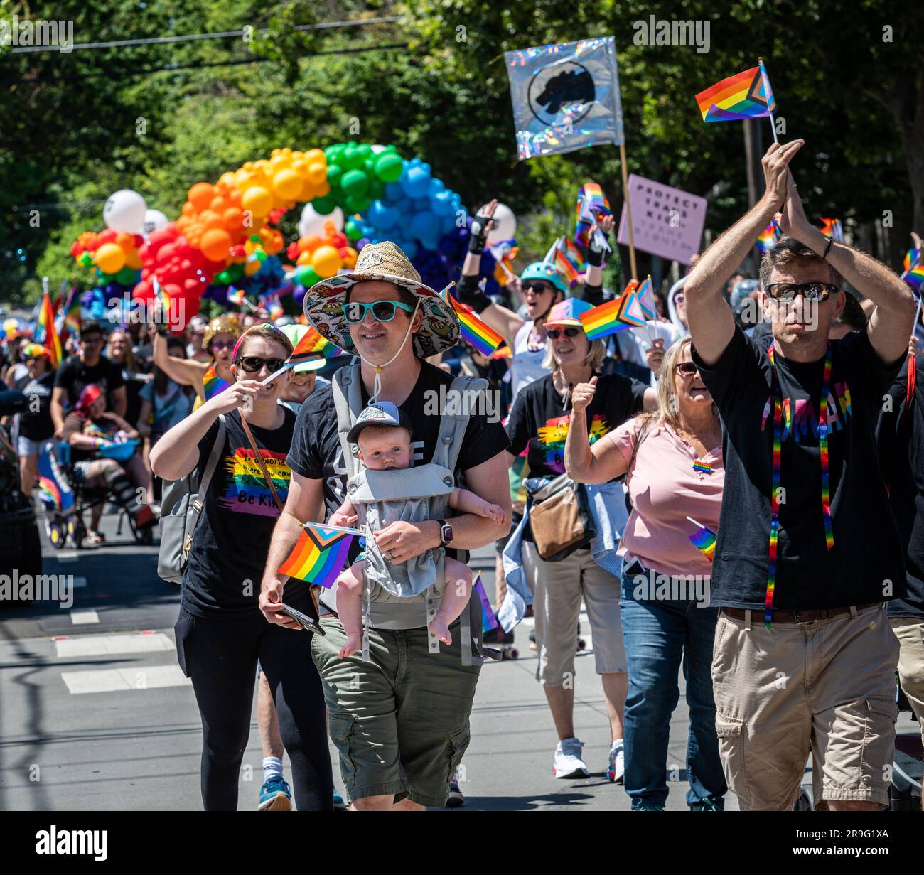 Foto eines Paradeteilnehmers mit der Progress Pride-Flagge und dem Baby, das während der jährlichen Pride-Parade der Stadt vor sich trägt. Stockfoto