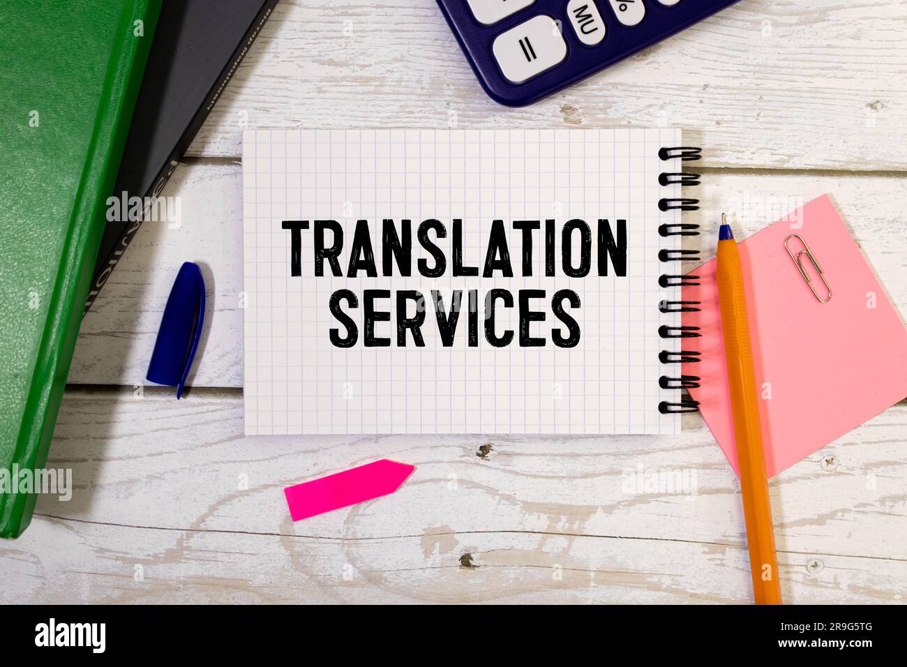 Auf hellem Hintergrund, goldgerahmte Gläser, eine Blume im Topf, ein grünes Notizbuch, ein roter Stift und ein braunes Notizbuch mit den TEXTÜBERSETZUNGSDIENSTEN. Bu Stockfoto