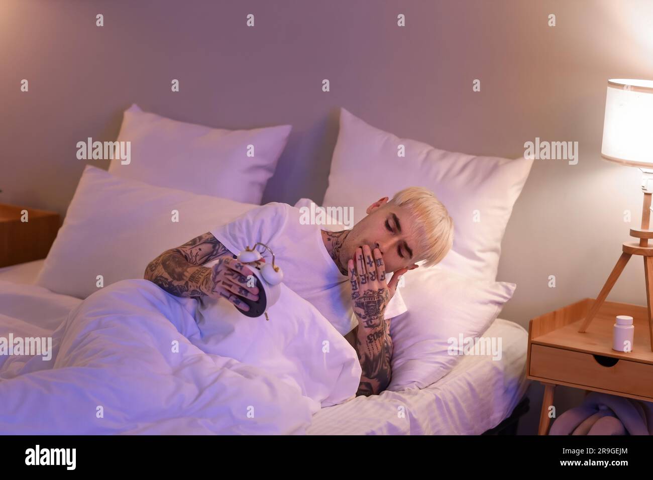 Ein tätowierter Mann beobachtet nachts die Zeit im Bett Stockfoto