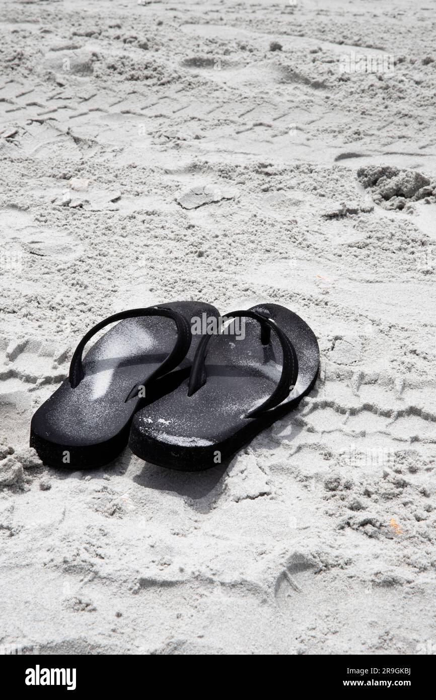 Schwarze Flip-Flops auf Sand, ruhiger, beruhigender Sandstrand Hintergrund mit Kopierbereich Stockfoto