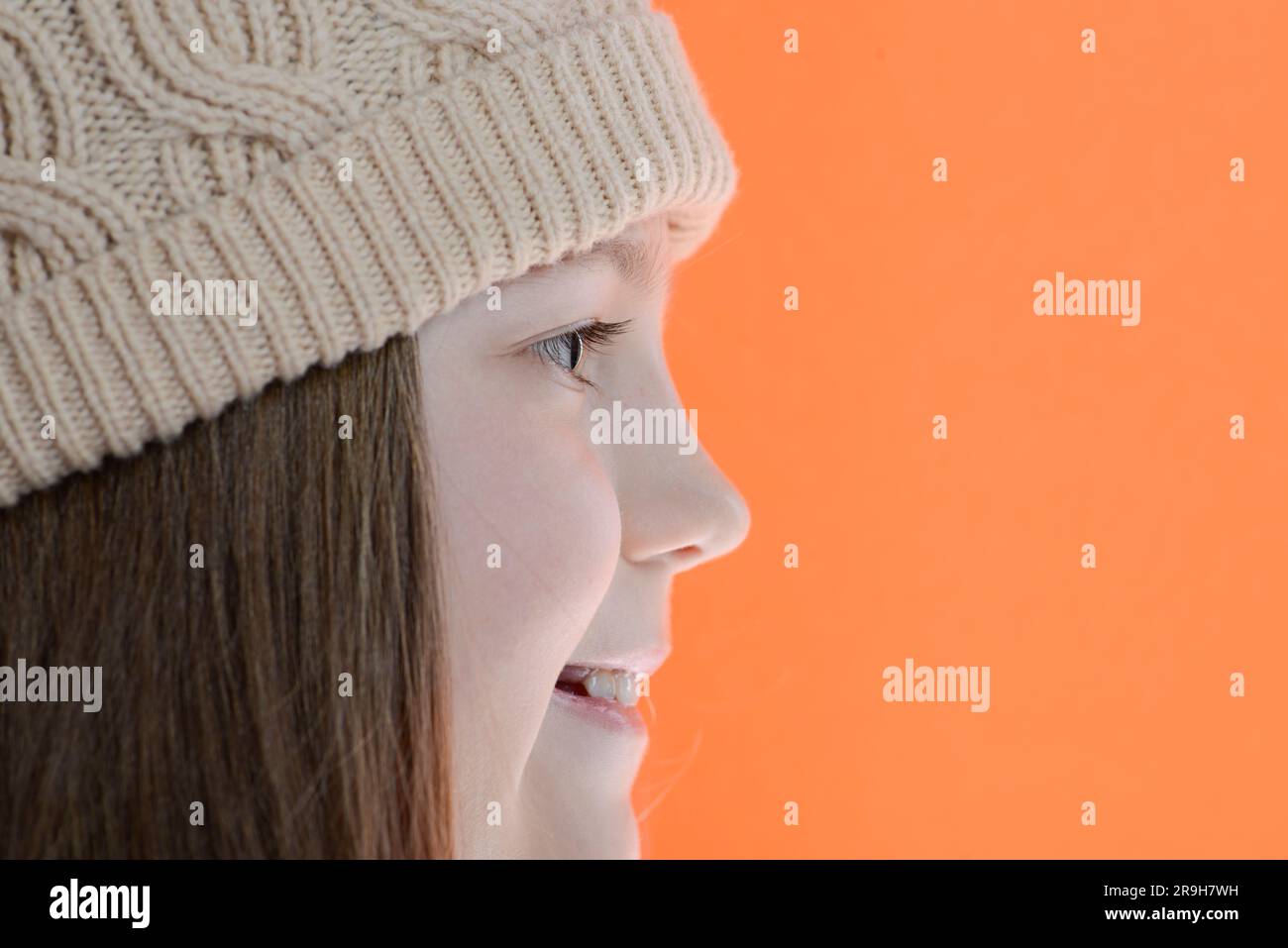 Lächelndes Mädchen in Mütze mit langen Haaren, Seitenansicht auf orangefarbenem Hintergrund Stockfoto