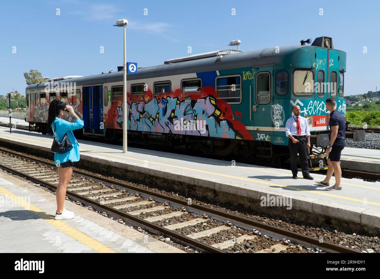 Der lokale Dieselmotor der Station Noto trenitalia ist mit Graffiti bedeckt und wartet auf dem Bahnsteig. Der Passagier spricht mit dem Bahnhofsvorsteher Stockfoto