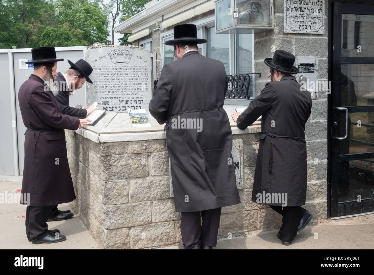 Vier jüdische Männer beten am Grabstein des Ribnitz Rebbe, da man annimmt, dass Gebete in der Nähe der Gerechten verstärkt werden. In Monsey New York. Stockfoto