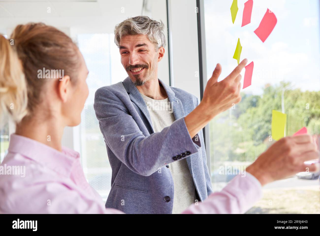 Ein fröhlicher Geschäftsmann, der über Haftnotizen mit einer Geschäftsfrau spricht Stockfoto
