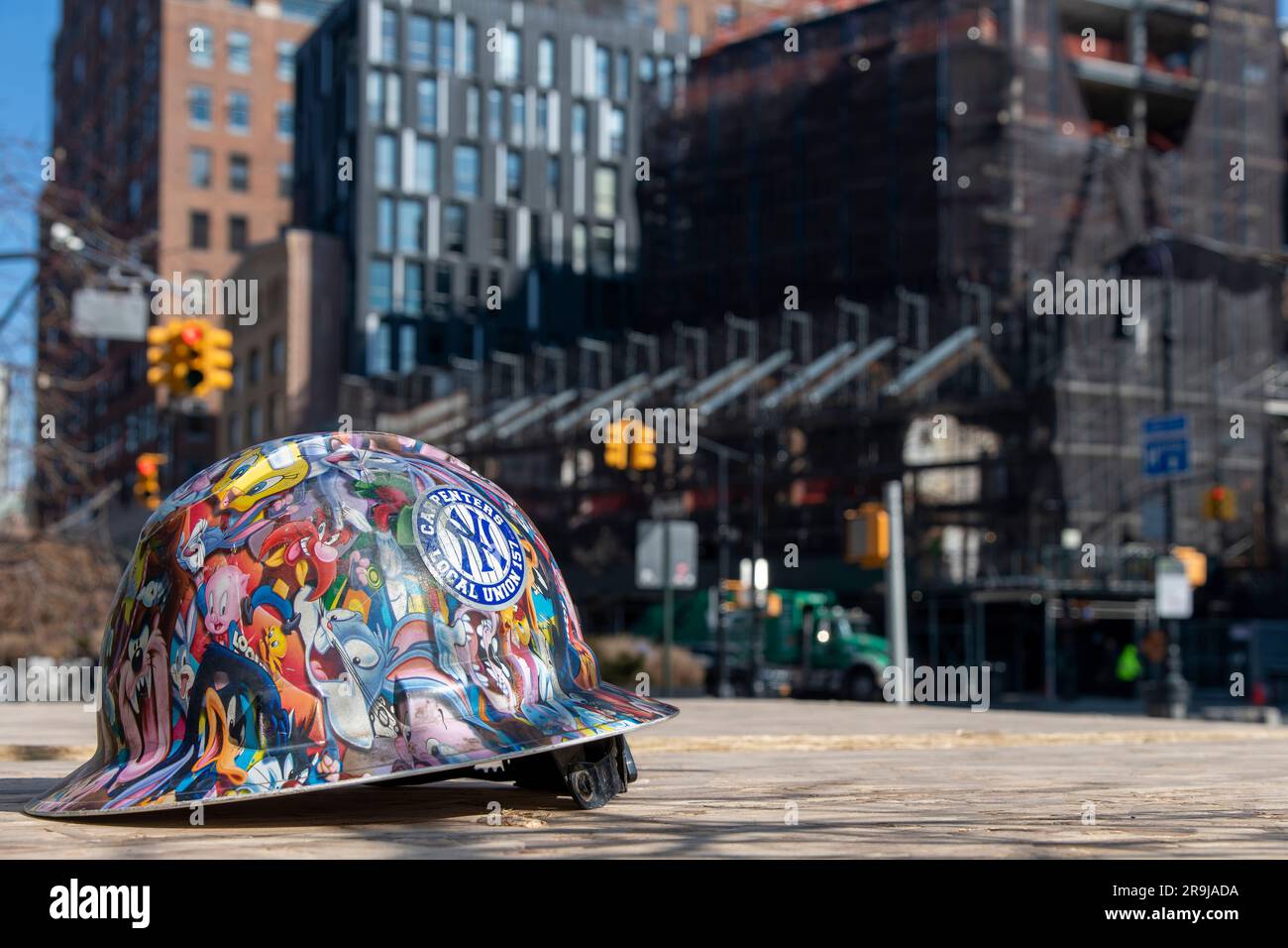New York City, NY, USA – April 2023; Nahaufnahme eines Schutzhelms gefüllt mit aufklebern von looney Tunes von einem Mitglied der lokalen Gewerkschaft des Zimmermanns mit Hintergrund von CI Stockfoto