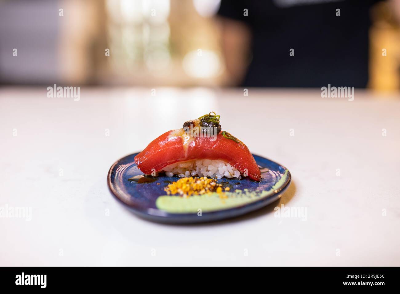 Nigiri-Sushi mit frischem Thunfischstück auf gekochtem Reis, garniert mit Sauce und serviert auf einem Holztisch gegen Verwischungen Stockfoto