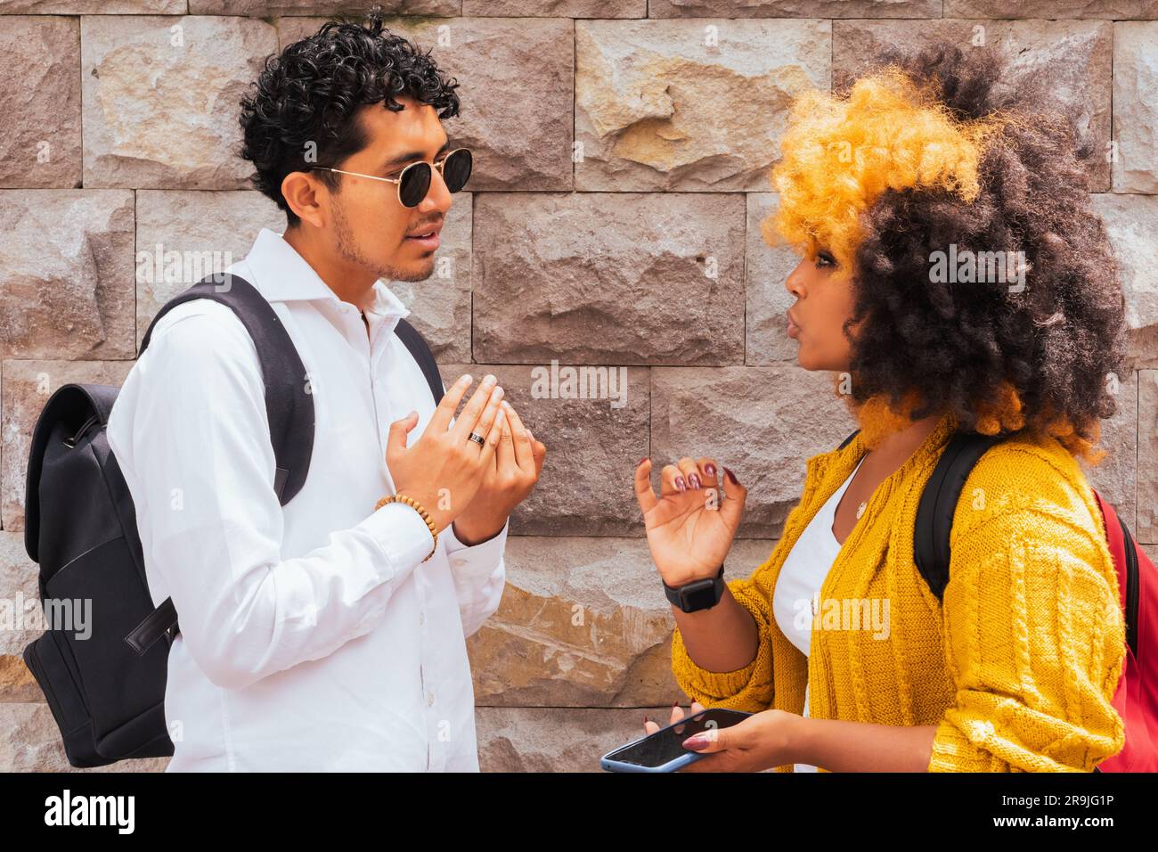 Vielfältiger Mann und Frau mit Afro-Haaren in lässiger Kleidung, die bei Tageslicht auf einer gepflasterten Straße an einer Steinwand stehen Stockfoto