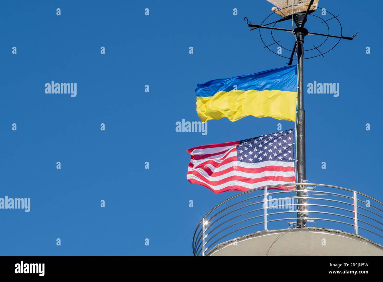 Die Flaggen der Ukraine und der USA flattern auf einem Fahnenmast vor einem blauen Himmel. Statussymbol. Ukrainische blaue und gelbe Flagge. Windtag im Freien. Stockfoto