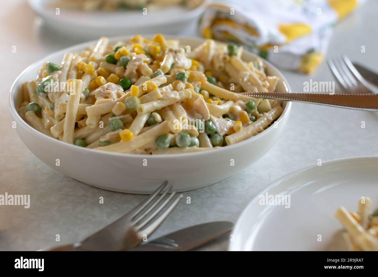 Nudelsalat mit Mayonnaise, Mais, grünen Erbsen, Schinken und gekochten Eiern in einer Schüssel Stockfoto