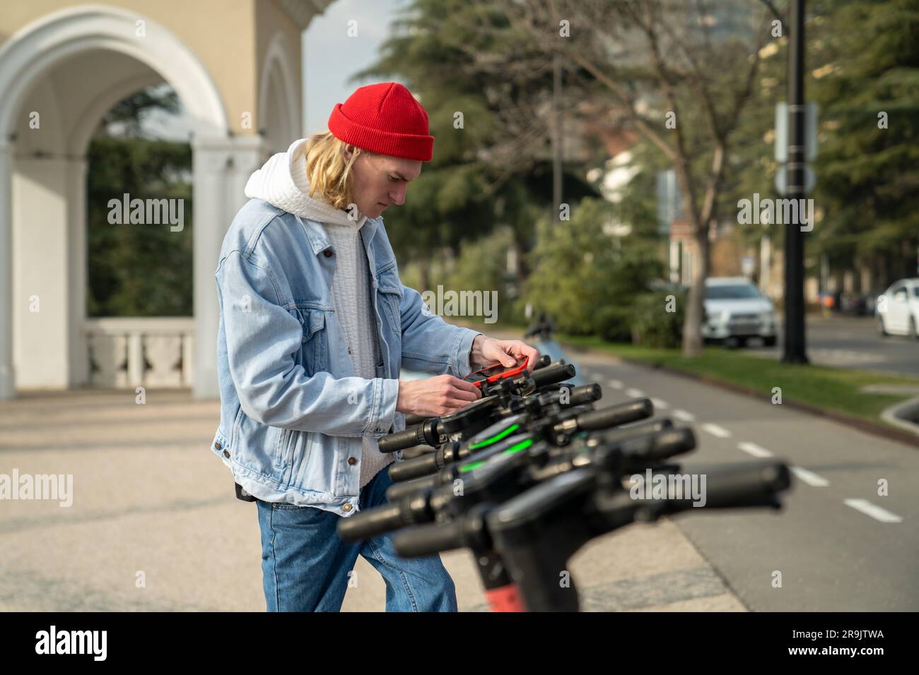 Der junge Mann installiert ein Handy auf einem gemieteten Roller. Man aktiviert den elektrischen Transport über das Smartphone Stockfoto