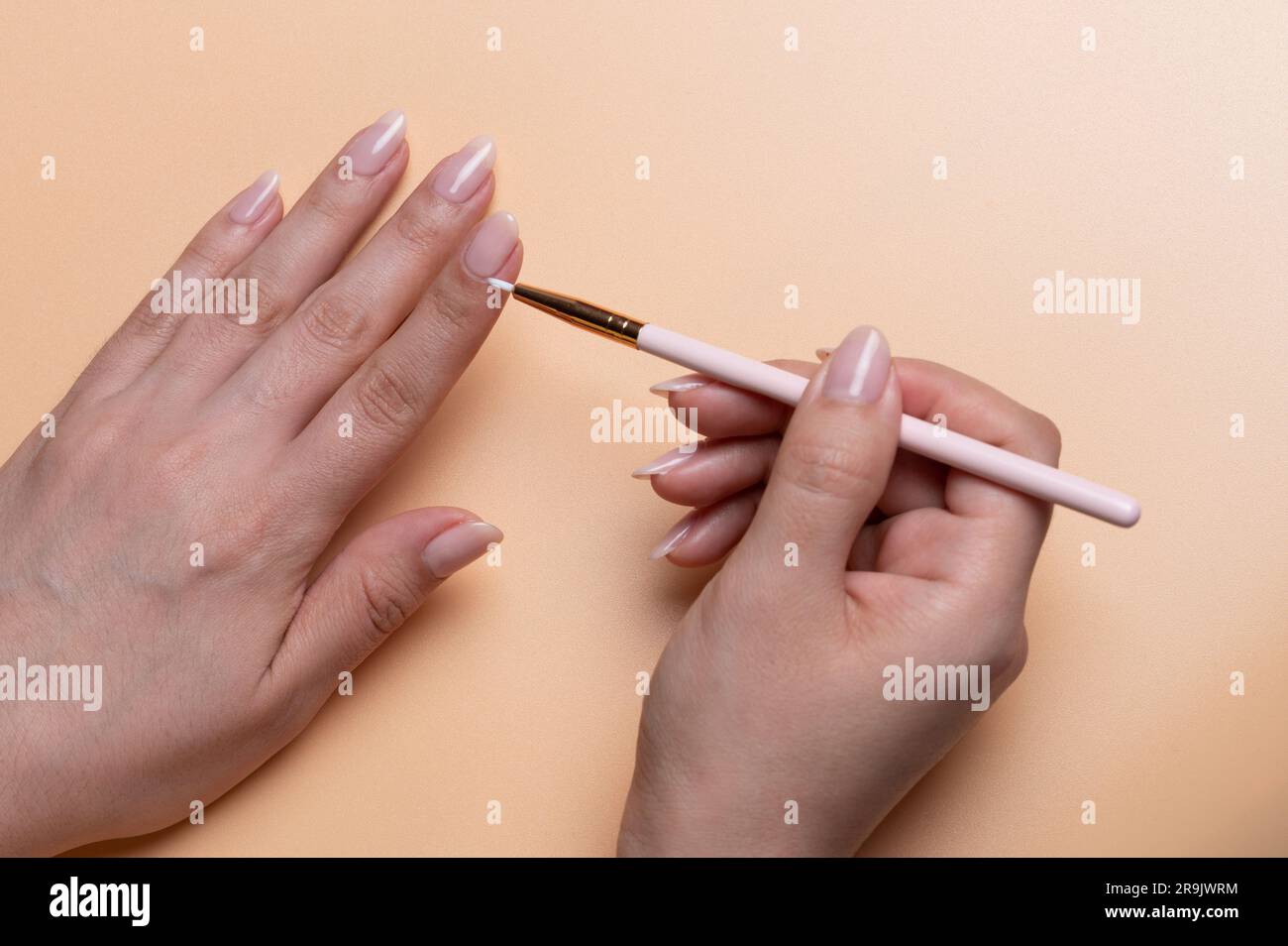Tragen Sie Nagelfarbe auf die Nahaufnahme der Frauenhand mit beigefarbenem Hintergrund auf Stockfoto