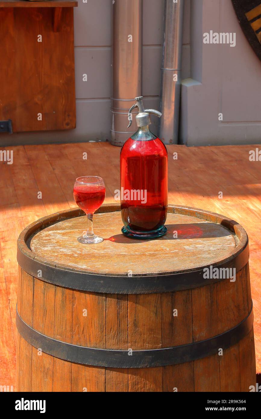 Auf dem Foto stehen ein alter Glasheber und ein Glas gefüllt mit einem Getränk aus roten Früchten auf einem Holzfass vor dem Eingang zum Café Lviv. Stockfoto