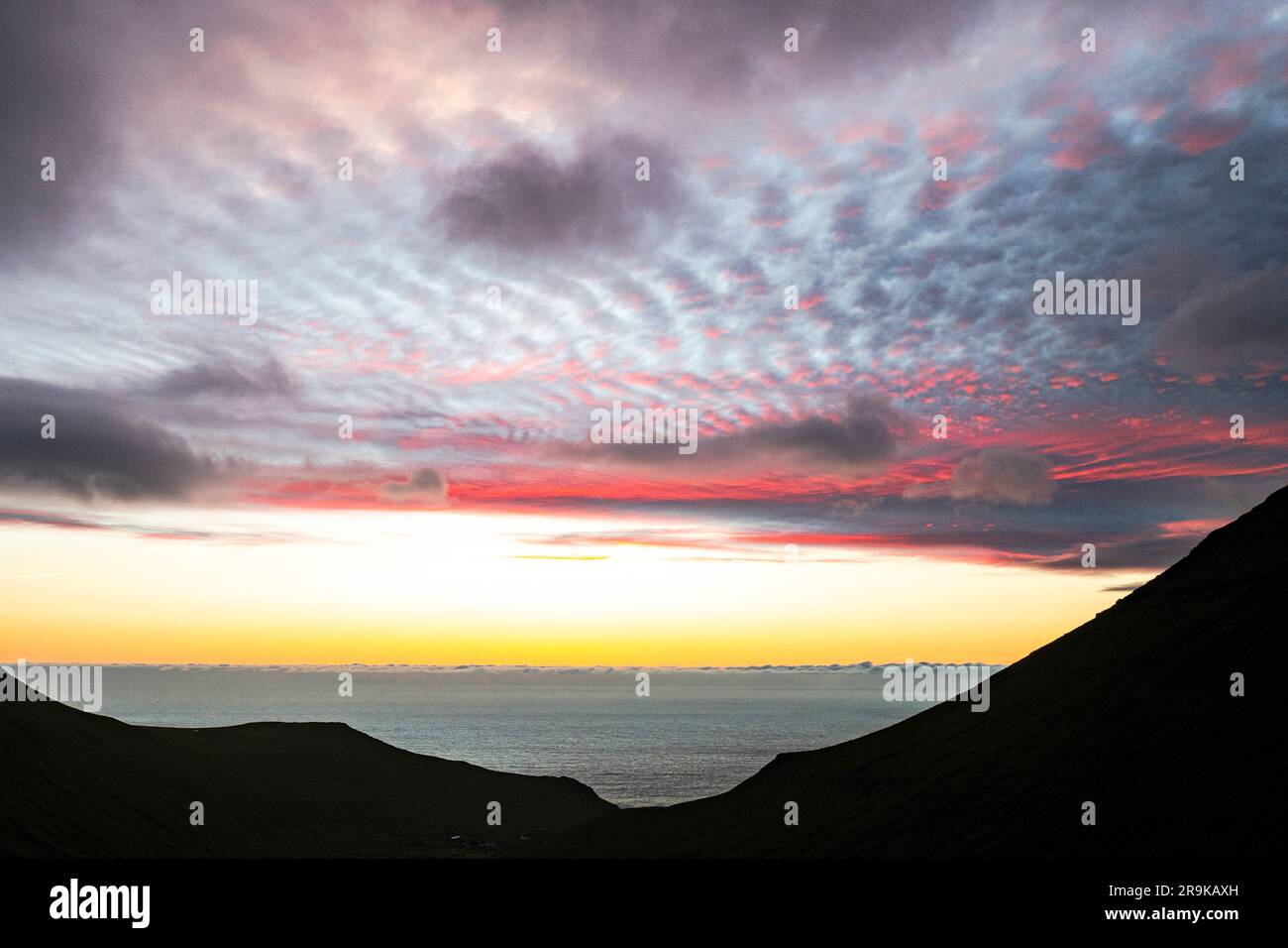 Malerische Wolken am Himmel bei Sonnenaufgang über den Silhouetten der Klippen rund um Gjogv, Eysturoy Island und die Färöer Inseln Stockfoto