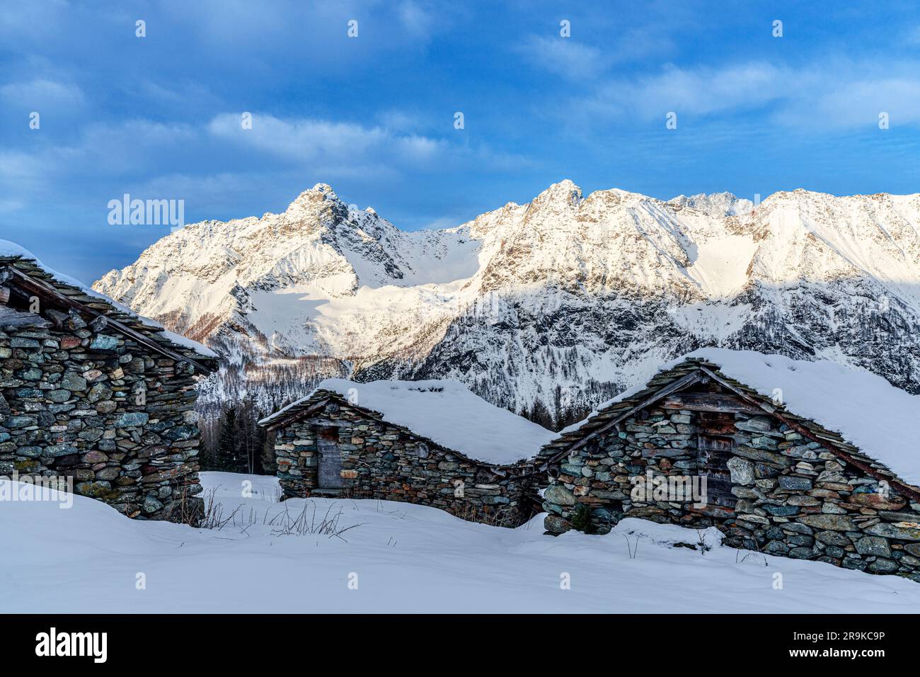 Schneebedeckte Berghütten mit schneebedeckten Gipfeln im Winter, Entova Alp, Valmalenco, Valtellina, Lombardei, Italien Stockfoto