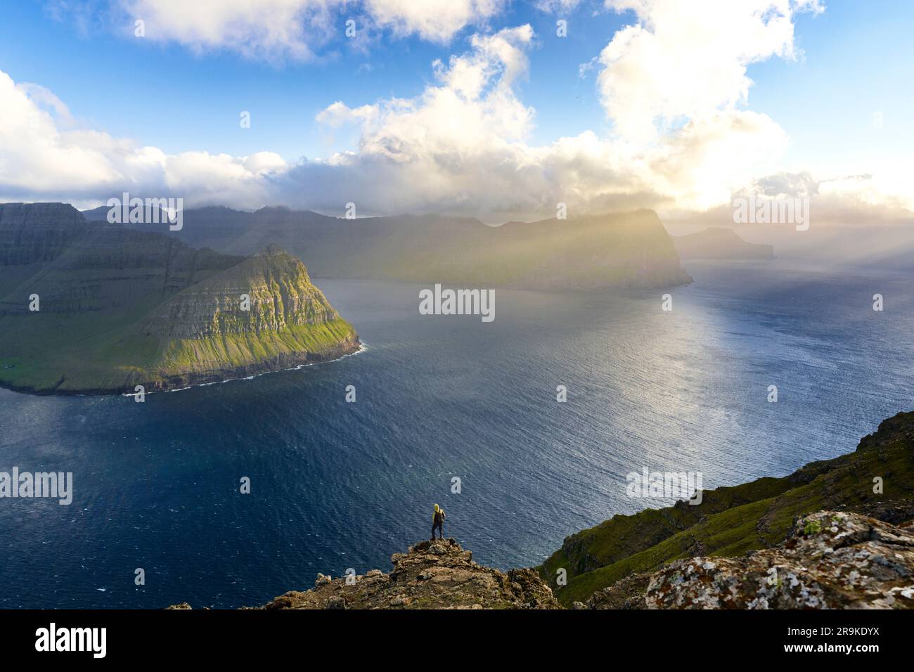 Blick aus der Vogelperspektive auf entfernte Wanderer auf Felsen mit Blick auf den Fjord im Sommer, Vidoy Island, Färöer Inseln Stockfoto