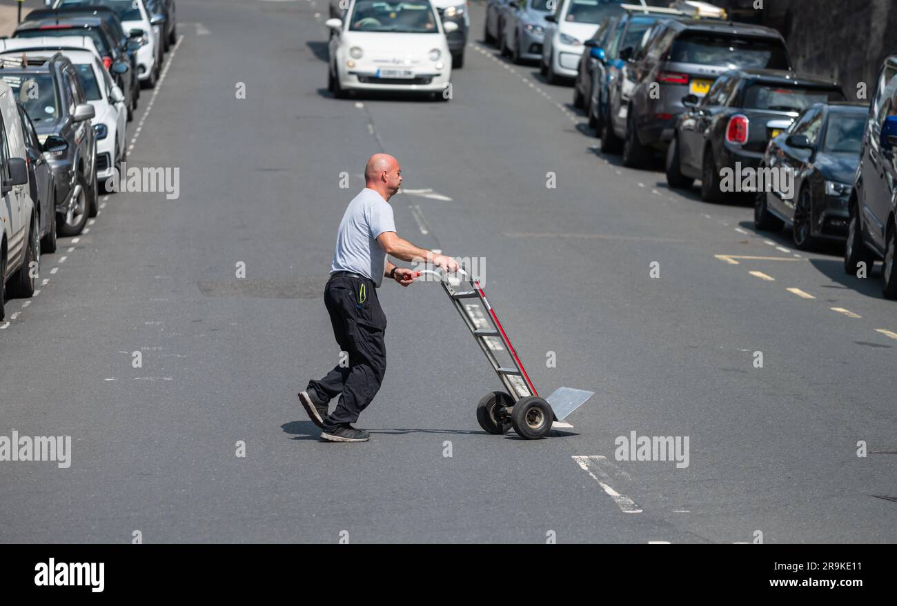 Lieferfahrer schiebt leeren Wagen über eine Straße, nachdem er Lebensmittel an einen Einzelhändler in England geliefert hat. Stockfoto