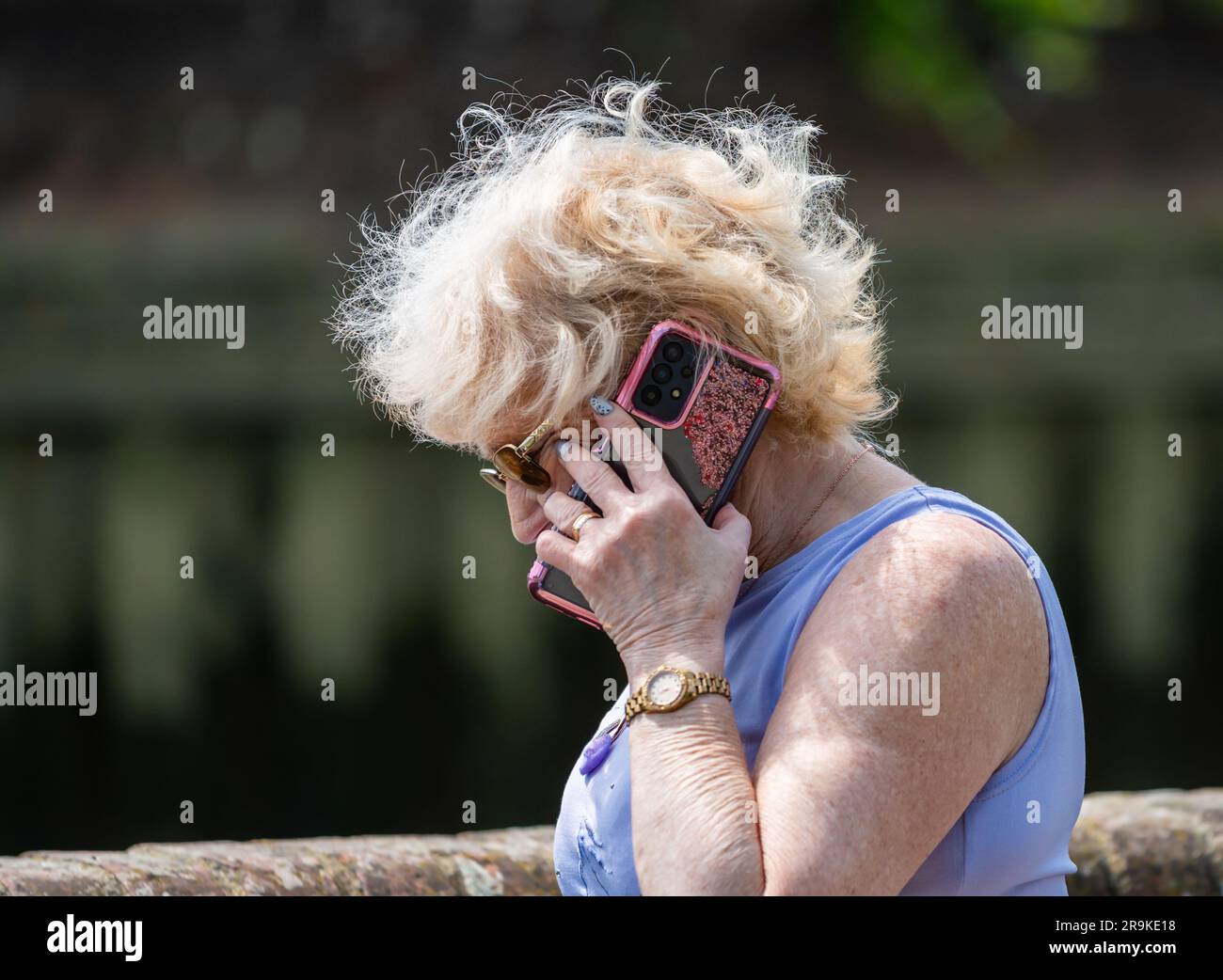 Ältere Frau steht draußen und spricht mit einem Handy, Handy oder Smartphone. Seniorin auf dem neuesten Stand in Sachen moderne Technologie, Großbritannien. Stockfoto