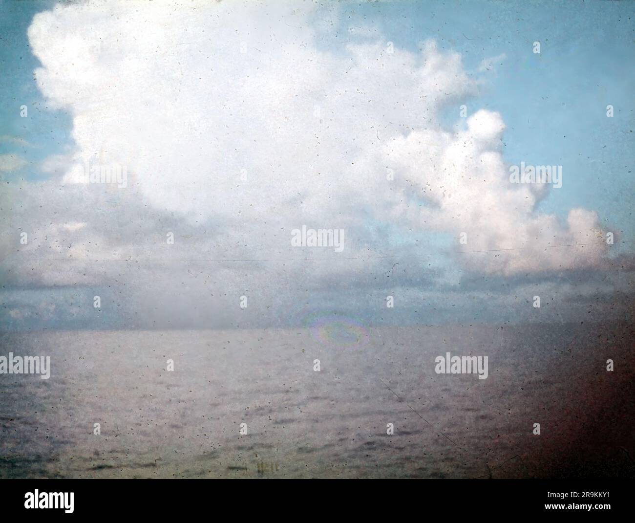 Klassische 8 mm 1950er Dia-Folie eines ruhigen Meeres mit flauschigen weißen Wolken, Staub und Kratzern Stockfoto
