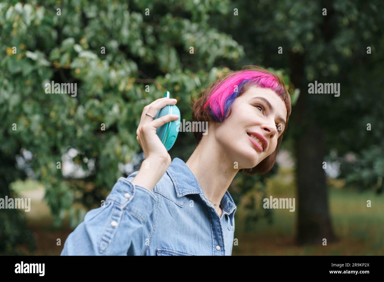 Ein Mädchen mit rosa Haaren sitzt im Park unter einem Baum mit einer Flasche Wasser und entspannt sich Stockfoto