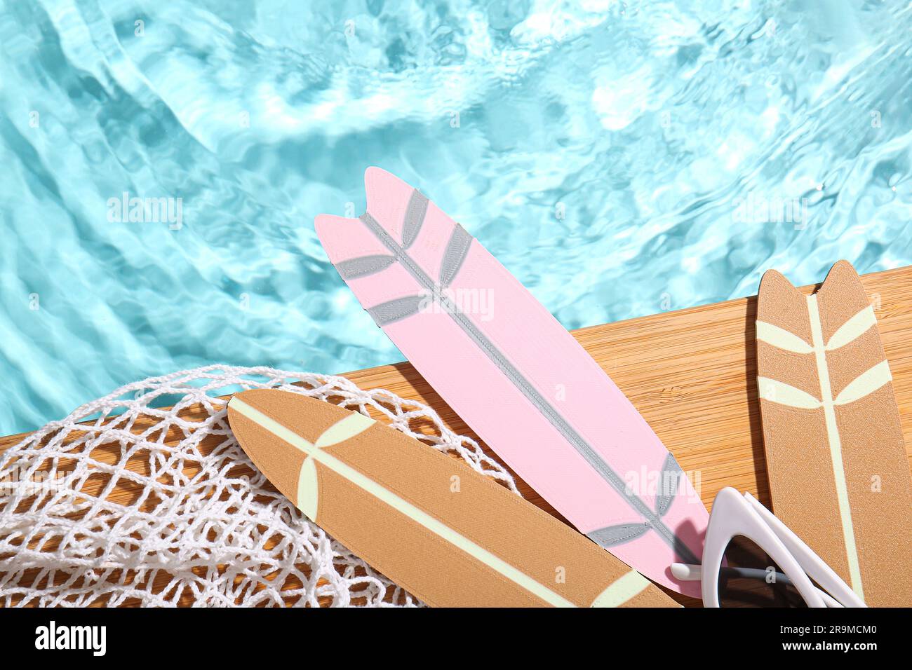 Komposition mit Mini-Surfbrettern, Netz und Sonnenbrille am Rand des Swimmingpools Stockfoto